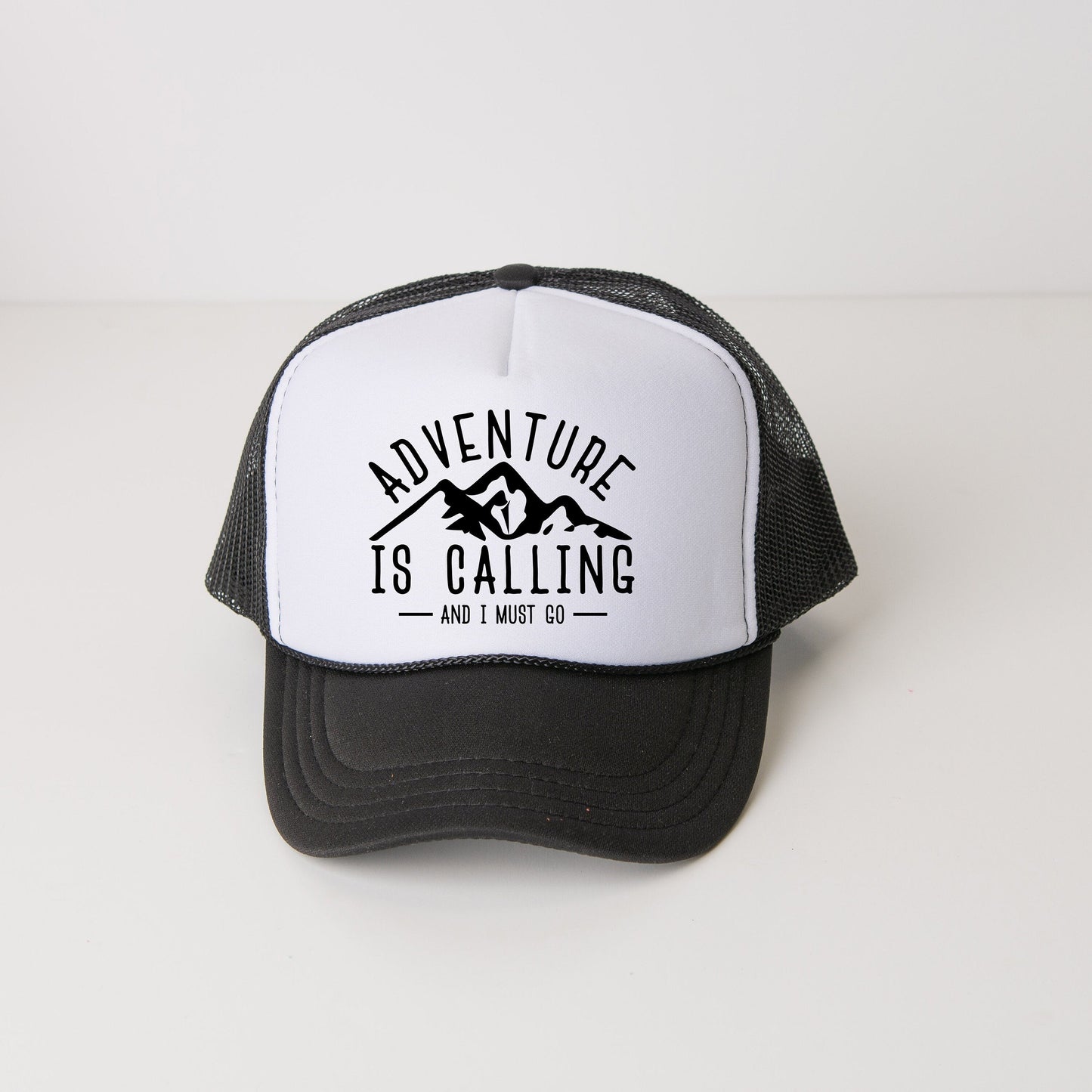 a black and white trucker hat with the words adventure is calling printed on it
